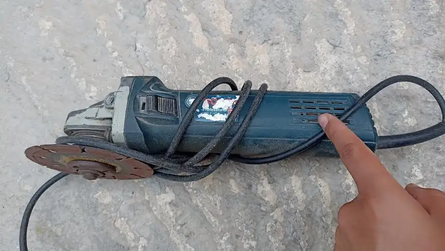 Primer plano de una mano técnica midiendo la tensión de una amoladora abierta en un banco de trabajo profesional, con herramientas de precisión al lado.