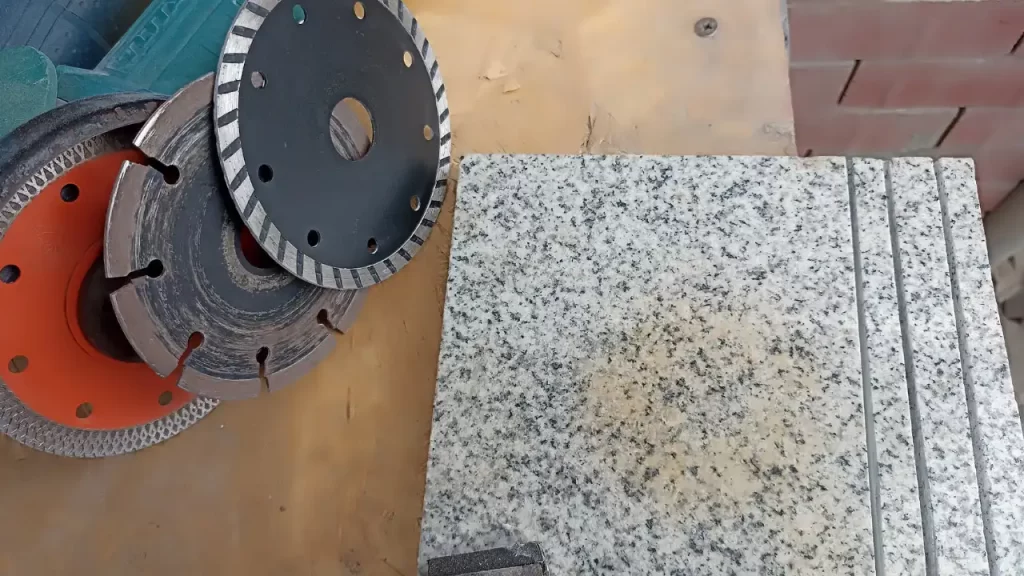 Un maestro marmolero utilizando una pulidora de agua sobre una placa de granito negro, con pads diamantados y equipo de seguridad visible.