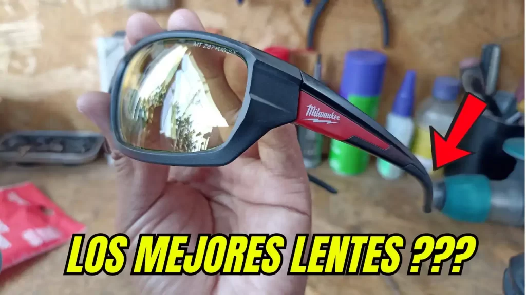 Primer plano de los lentes de seguridad Milwaukee modelo 48-73-2121 con cristales amarillos y logotipo de Milwaukee en la patilla, sobre un banco de herramientas profesional.